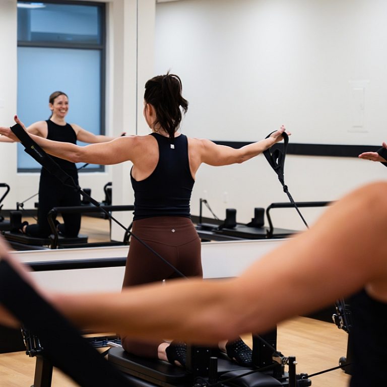 MVP Reformer Pilates, Woman on reformer, arms in straps with arms out